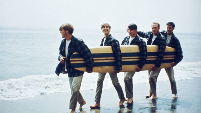 American Rock and roll band The Beach Boys walk along a beach holding a surfboard during a photoshoot for their debut album, 'Surfin' Safari', Los Angeles, California, August 1962. Left to right: Dennis Wilson, David Marks, Carl Wilson, Mike Love and Brian Wilson. (Photo by Michael Ochs Archives/Getty Images)